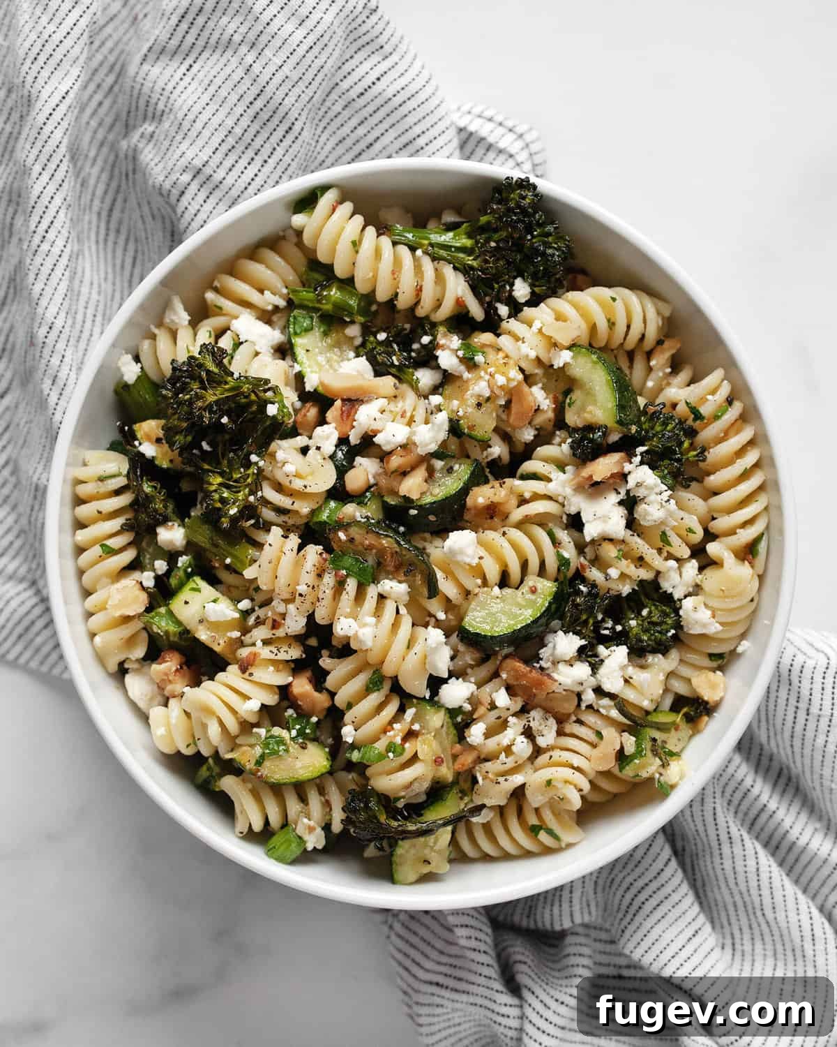 Rustic Roasted Broccolini Zucchini Pasta Salad 7 A large, inviting serving bowl filled with the vibrant roasted broccolini and zucchini pasta salad, garnished generously with fresh herbs and crumbled feta cheese.