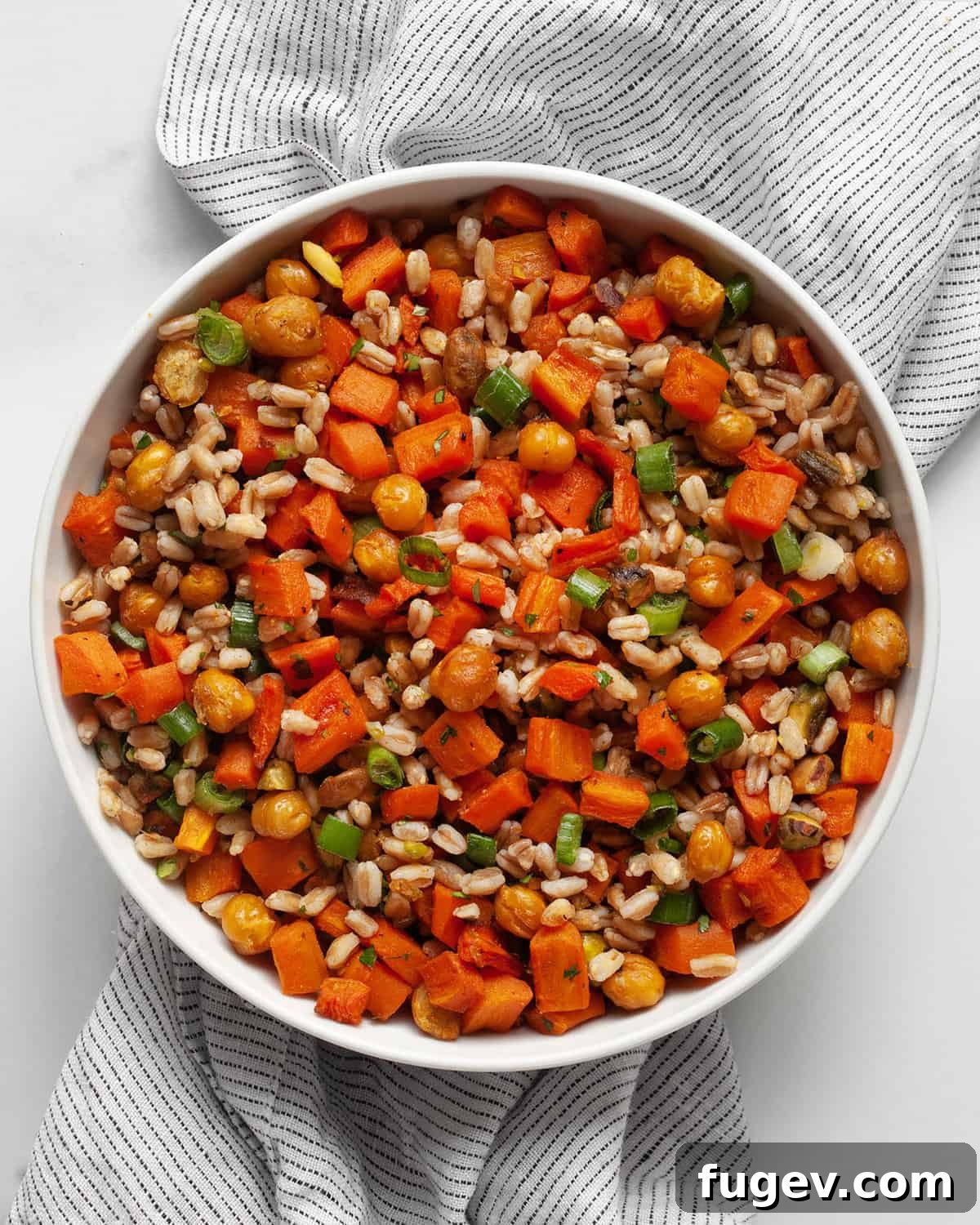 Caramelized Carrot Farro 2 A vibrant bowl of farro with roasted carrots and chickpeas, garnished with fresh herbs.