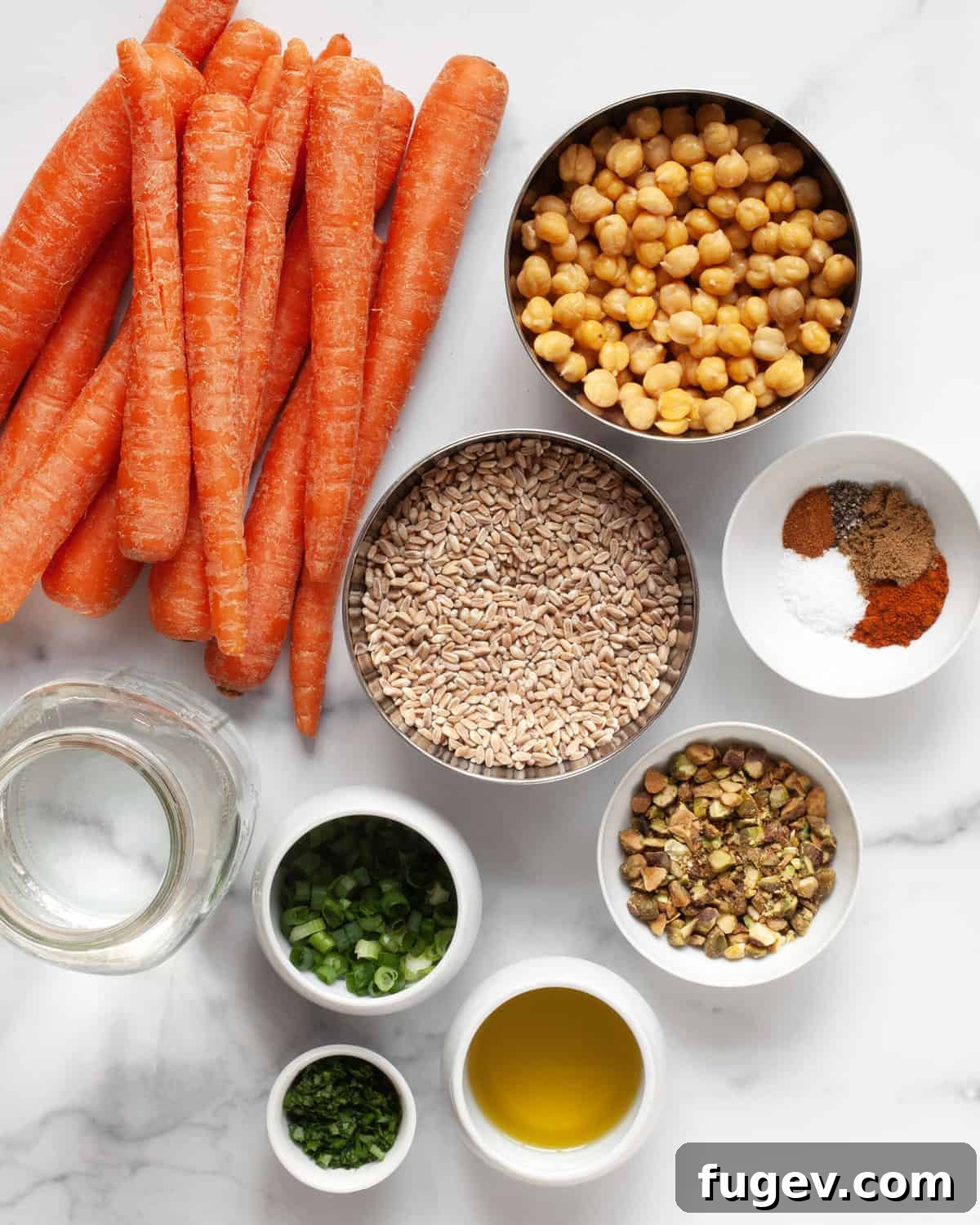 Caramelized Carrot Farro 3 A collection of fresh ingredients including carrots, chickpeas, farro, scallions, parsley, pistachios, olive oil, and a selection of spices.
