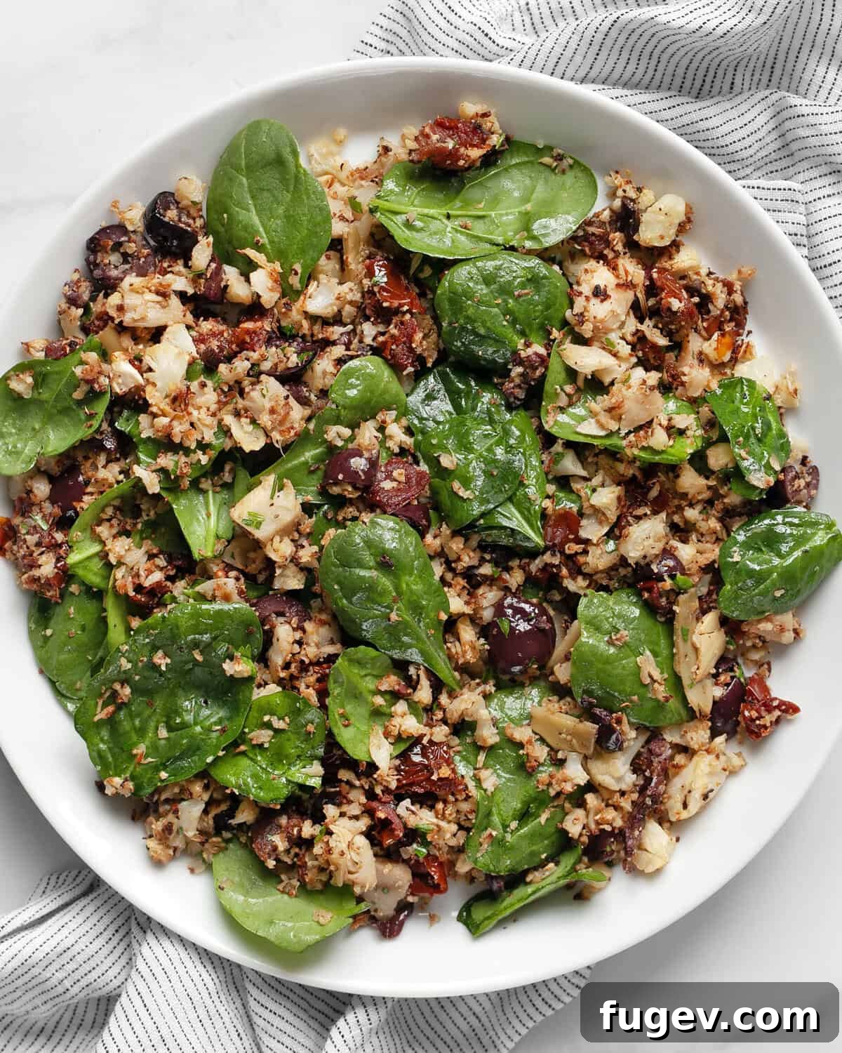 Crisp Roasted Cauliflower Grains 2 Roasted cauliflower rice with sun dried tomatoes, olives, artichokes and spinach on a plate, garnished with fresh herbs.