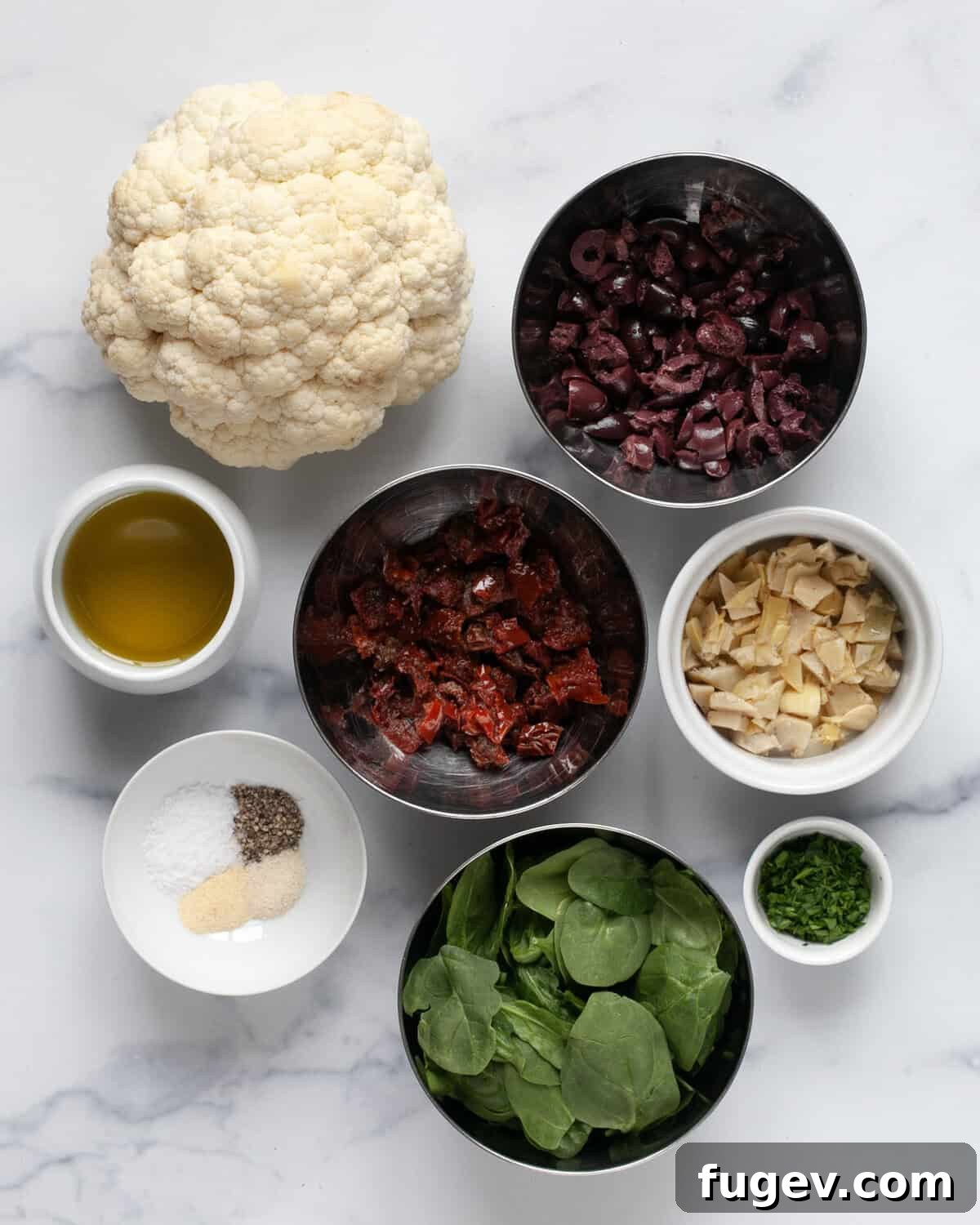 Crisp Roasted Cauliflower Grains 3 Ingredients for roasted cauliflower rice, including a whole cauliflower head, sun-dried tomatoes, olives, artichoke hearts, fresh spinach, olive oil, and dried spices.