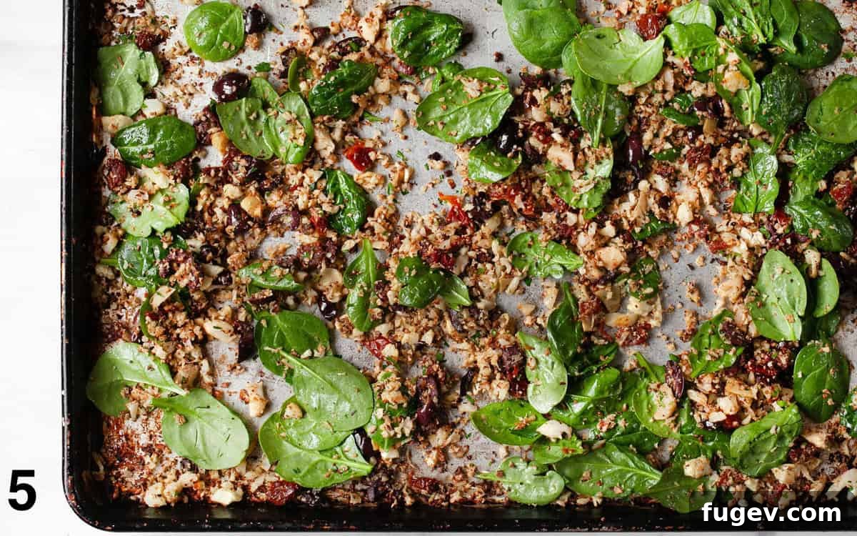 Crisp Roasted Cauliflower Grains 6 Finished roasted cauliflower rice stirred with sun-dried tomatoes, olives, artichokes, and wilted spinach on a baking sheet.