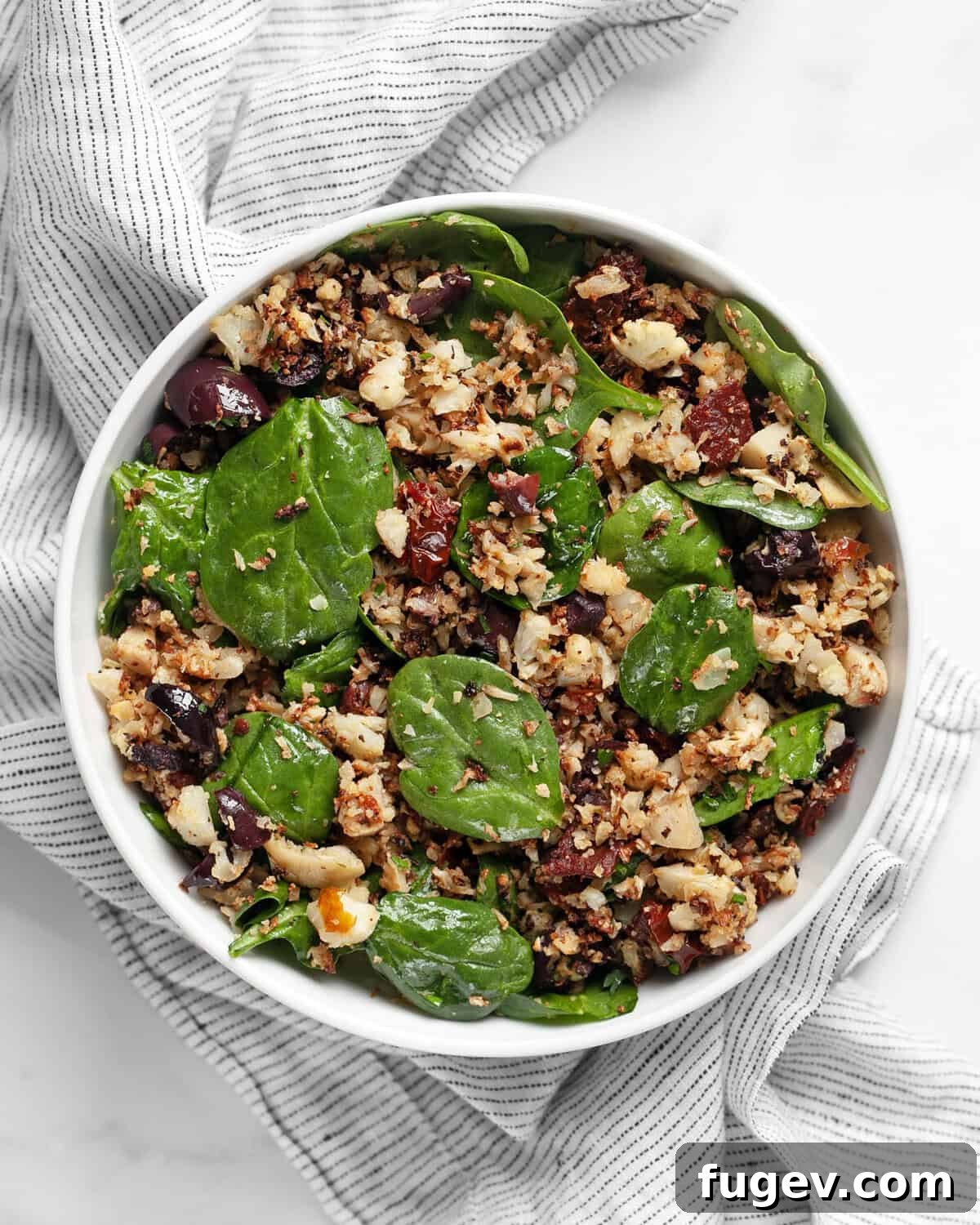 Crisp Roasted Cauliflower Grains 7 A bowl of roasted cauliflower rice with sun dried tomatoes, olives, artichokes, and spinach, garnished with fresh herbs.
