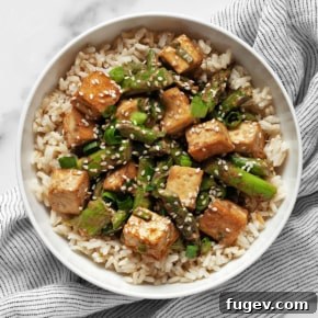 Sesame tofu and asparagus served over brown rice in a bowl, garnished with sesame seeds