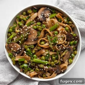 Colorful udon noodle stir-fry with bright green asparagus, sliced mushrooms, and peas in a bowl