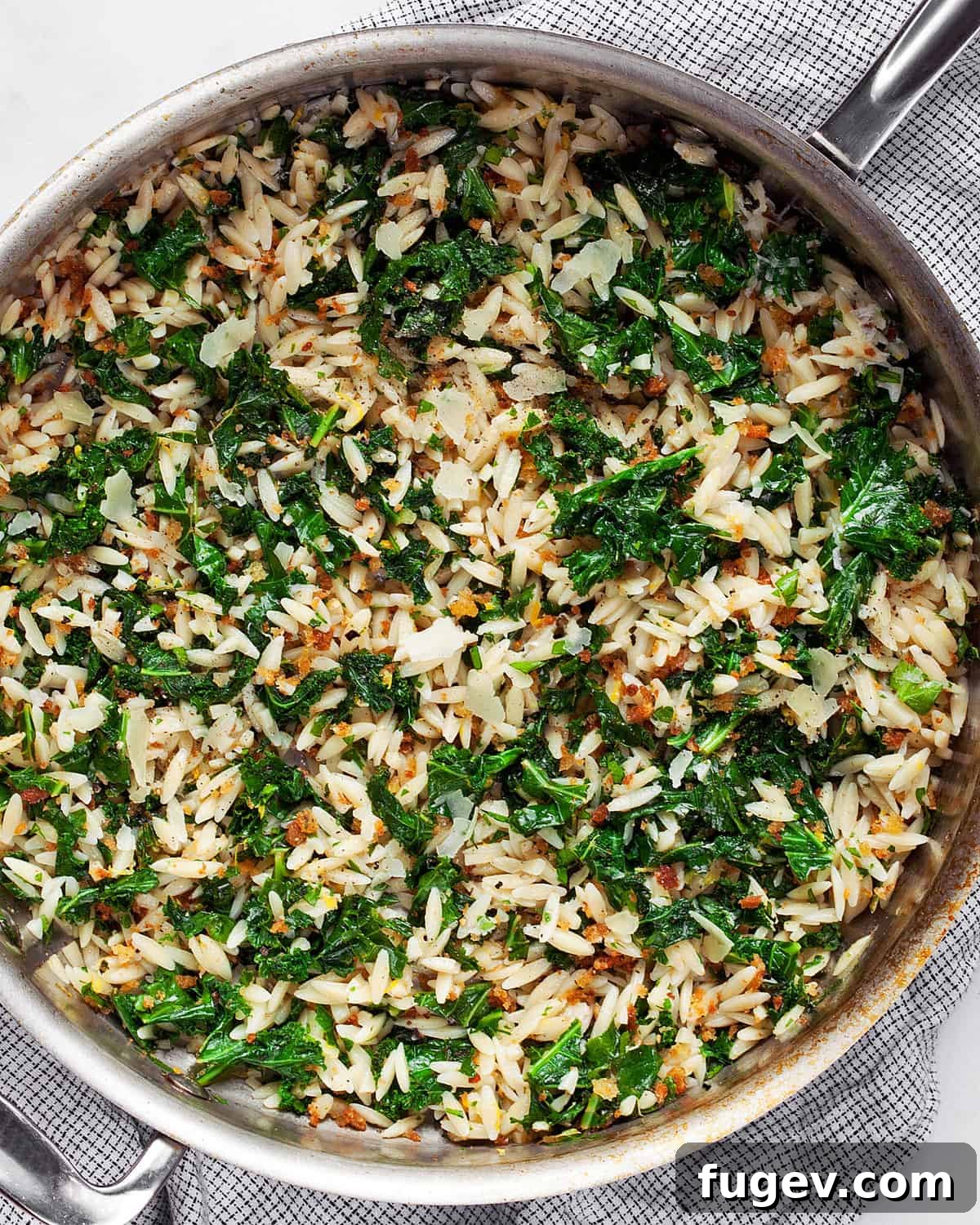 Zesty Lemon Kale Orzo 6 A serving of Lemon Kale Orzo in a rustic skillet, garnished with fresh parsley and lemon wedges, ready to be enjoyed.