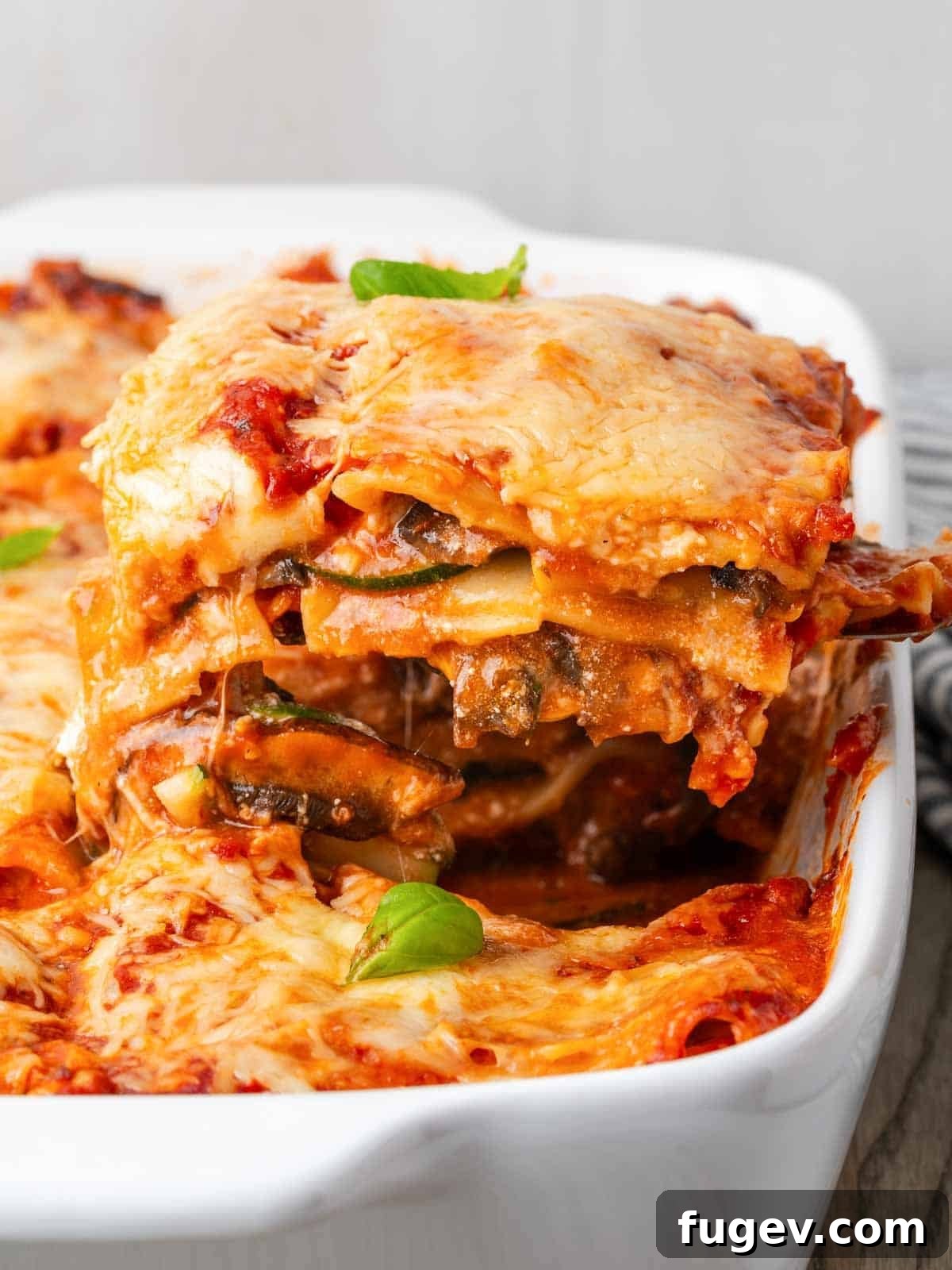 Vibrant Veggie Lasagna 2 A perfectly sliced piece of homemade vegetable lasagna, showing layers of pasta, vegetables, cheese, and sauce, resting on a white serving dish.
