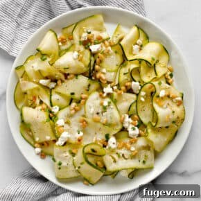 Elegant raw zucchini ribbons salad on a white plate, garnished with fresh herbs and pine nuts.