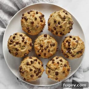 A plate featuring seven warm chocolate chip zucchini muffins, lightly spiced.