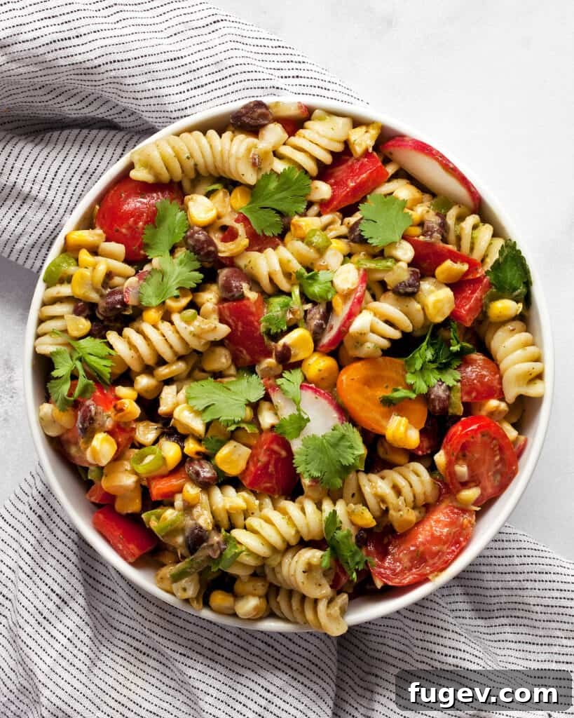 Fiesta Pasta Salad 2 A large bowl filled with vibrant Southwest Pasta Salad, featuring fusilli pasta, grilled corn kernels, black beans, diced red bell peppers, halved cherry tomatoes, and sliced radishes, all coated in a creamy green avocado-lime dressing.