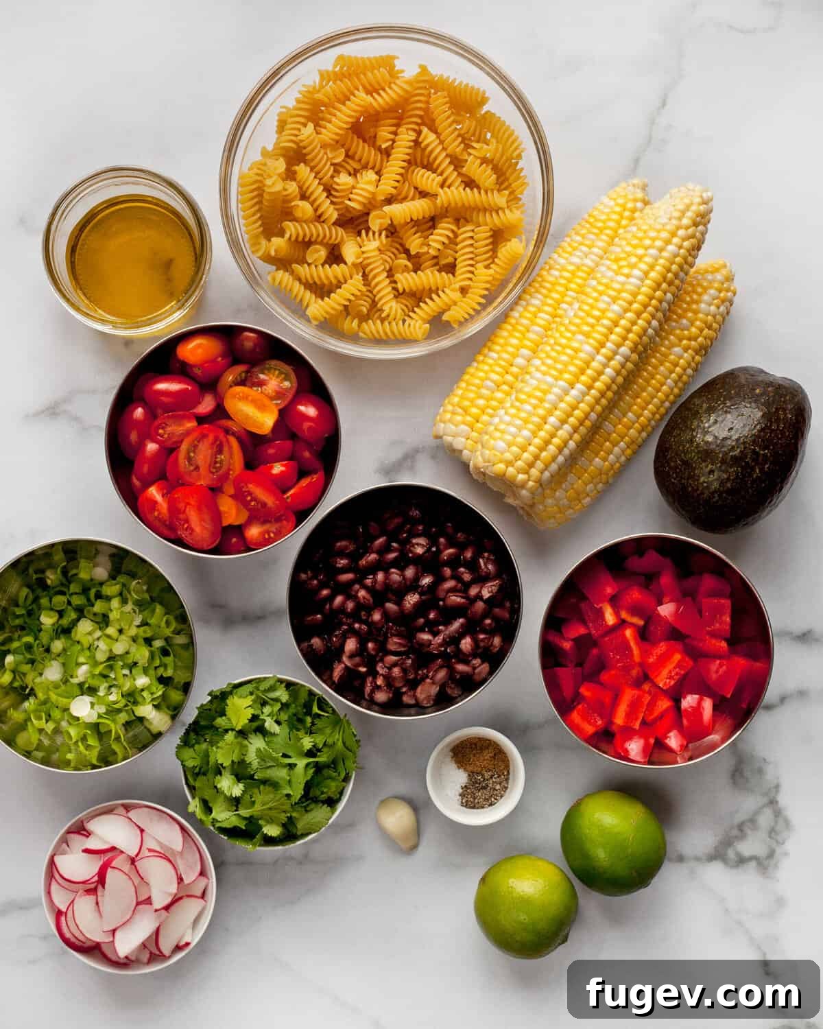Fiesta Pasta Salad 3 A flat lay photograph showcasing all the fresh ingredients for Southwest Pasta Salad laid out on a surface: uncooked fusilli pasta, three ears of corn, a can of black beans, a pint of grape tomatoes, a red bell pepper, radishes, scallions, a bunch of cilantro, a ripe avocado, limes, and a bottle of olive oil.