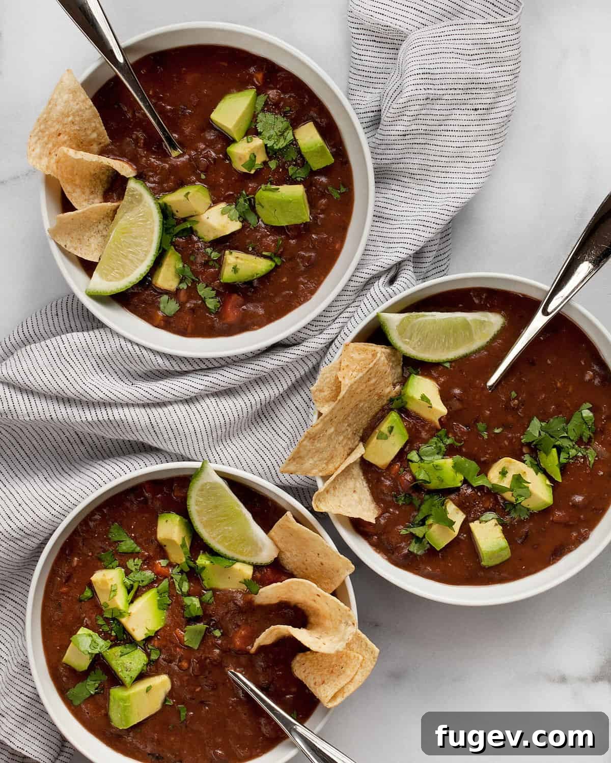 Smoky Vegan Black Bean Comfort 2 Three bowls of black bean soup topped with fresh avocados, cilantro, and lime wedges, showcasing its vibrant presentation.