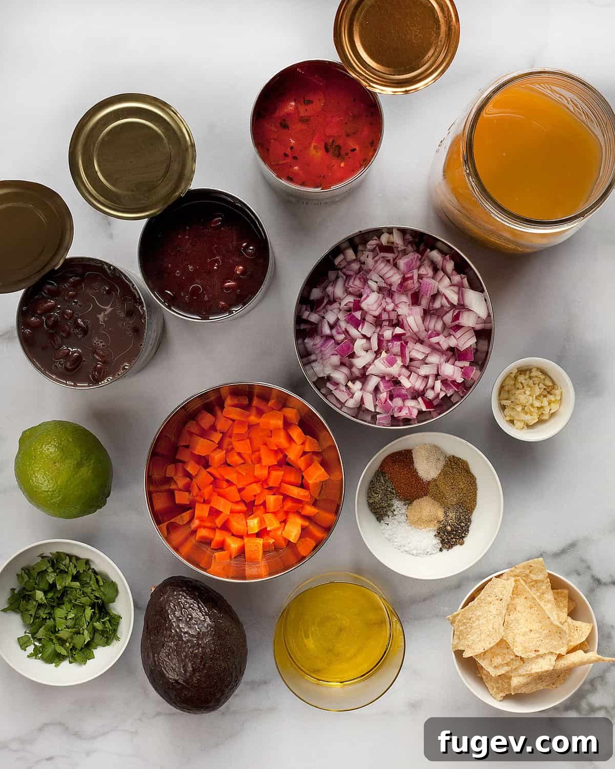 Smoky Vegan Black Bean Comfort 3 A vibrant flat lay of black bean soup ingredients including canned beans, carrots, red onions, tomatoes, garlic, and a variety of dried spices.