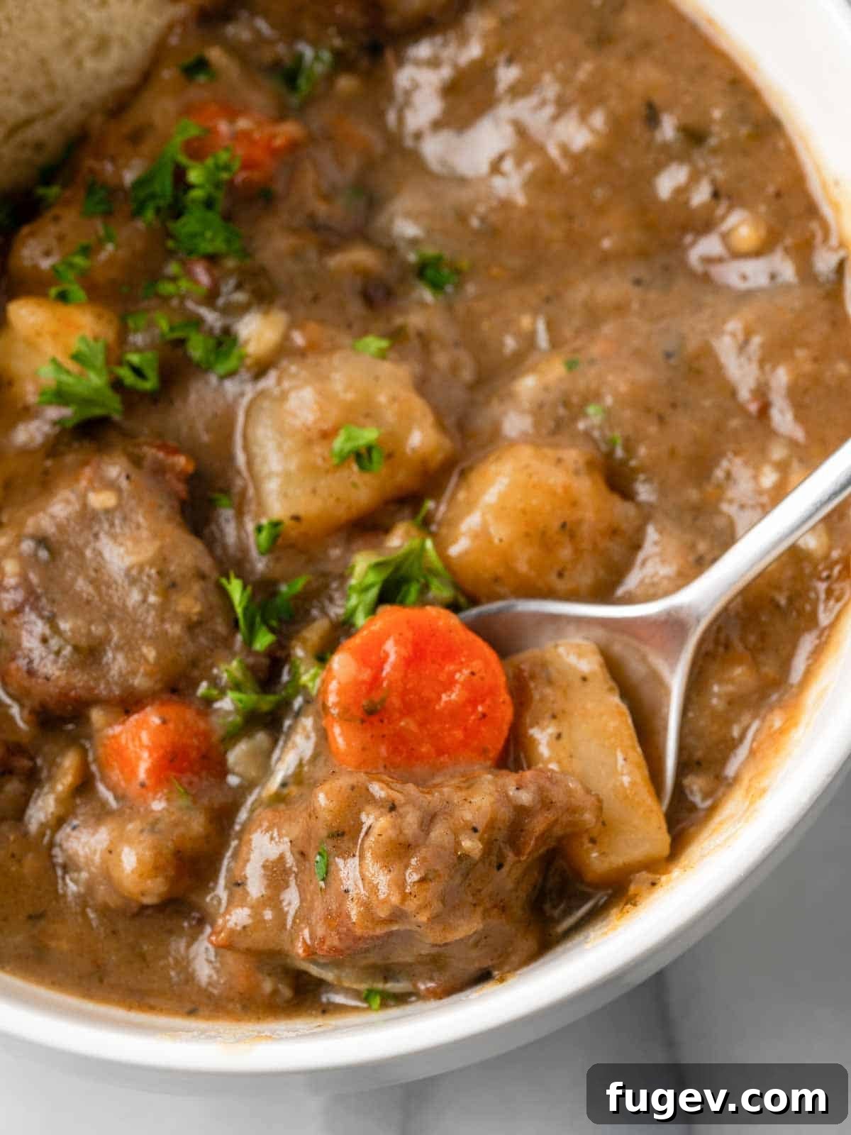 Classic Cast Iron Beef Stew 2 Closeup of rich beef stew with carrots and beef chunks on a spoon, ready to be enjoyed.