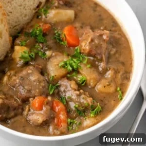 Hearty beef stew with tender beef, carrots, and a sprinkle of fresh parsley in a white bowl.