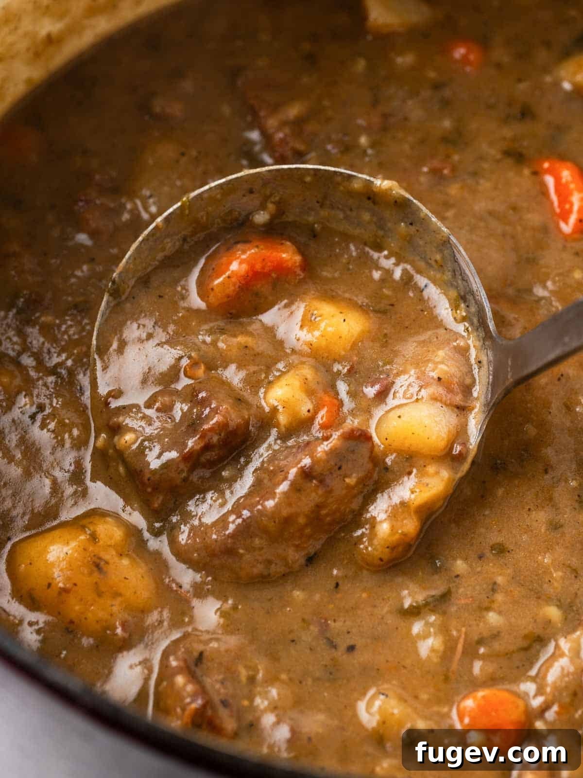Classic Cast Iron Beef Stew 4 Scoop of beef stew being lifted from a Dutch oven with a ladle, showcasing the rich broth and tender ingredients.