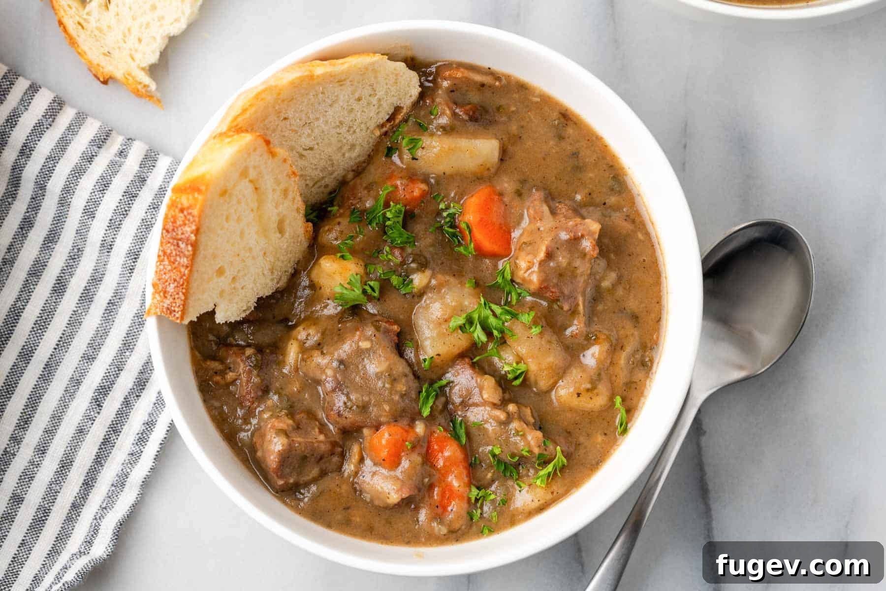 Classic Cast Iron Beef Stew 6 A serving of beef stew in a white bowl, garnished with fresh parsley and accompanied by a slice of crusty bread.
