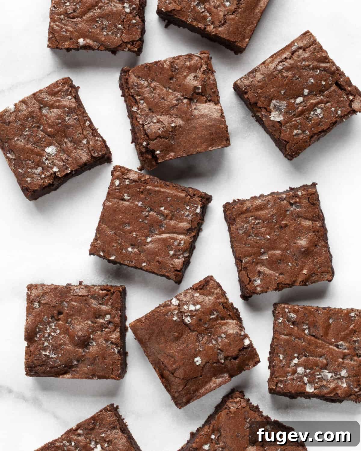 Effortless Salted Fudge Brownies 2 Perfectly cut brownie squares on a marble board, garnished with flaky sea salt.