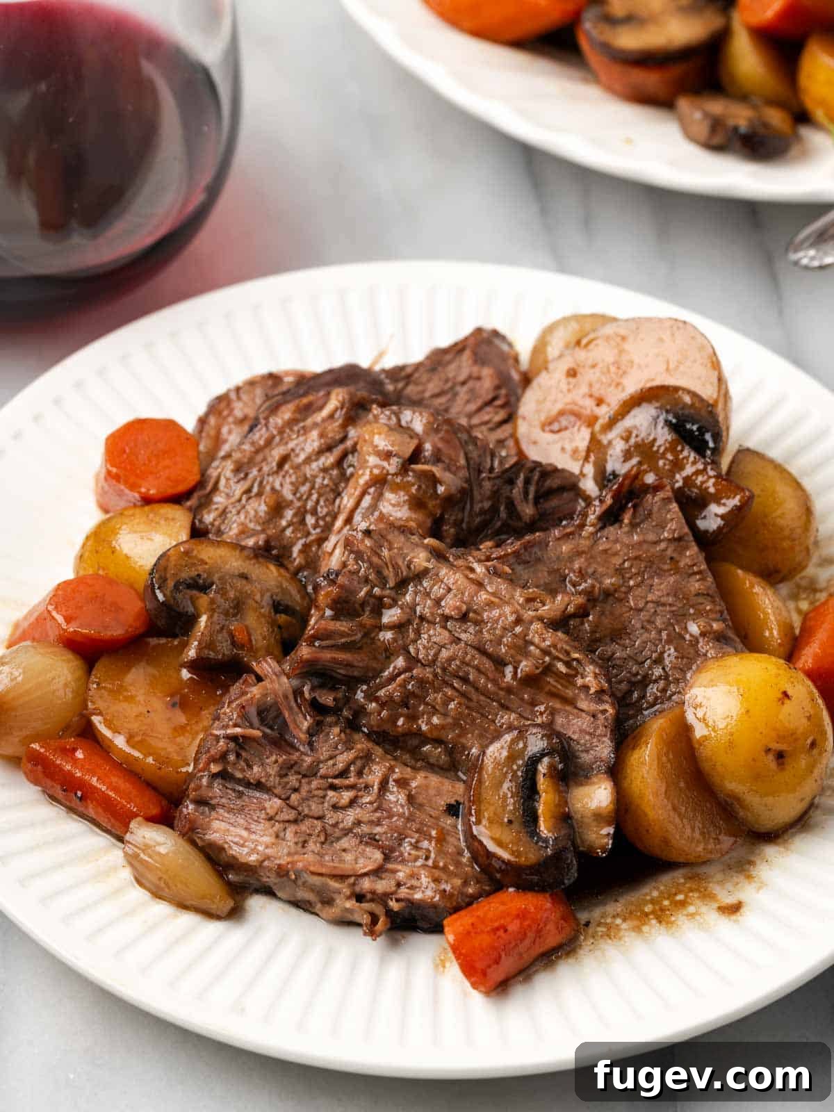 Serving Suggestion for Dutch Oven Pot Roast Perfectly sliced pot roast on a white plate, showcasing tender beef and colorful vegetables.