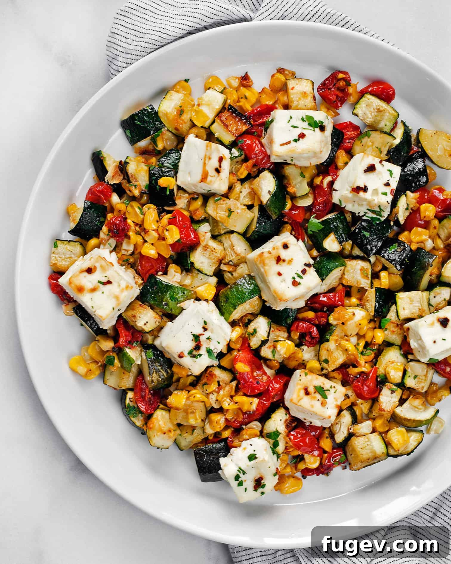 Tek Tepside Fırınlanmış Feta ve Sebzeler 2 A vibrant plate of baked feta with roasted zucchini, corn, and tomatoes, showcasing a healthy and colorful meal.