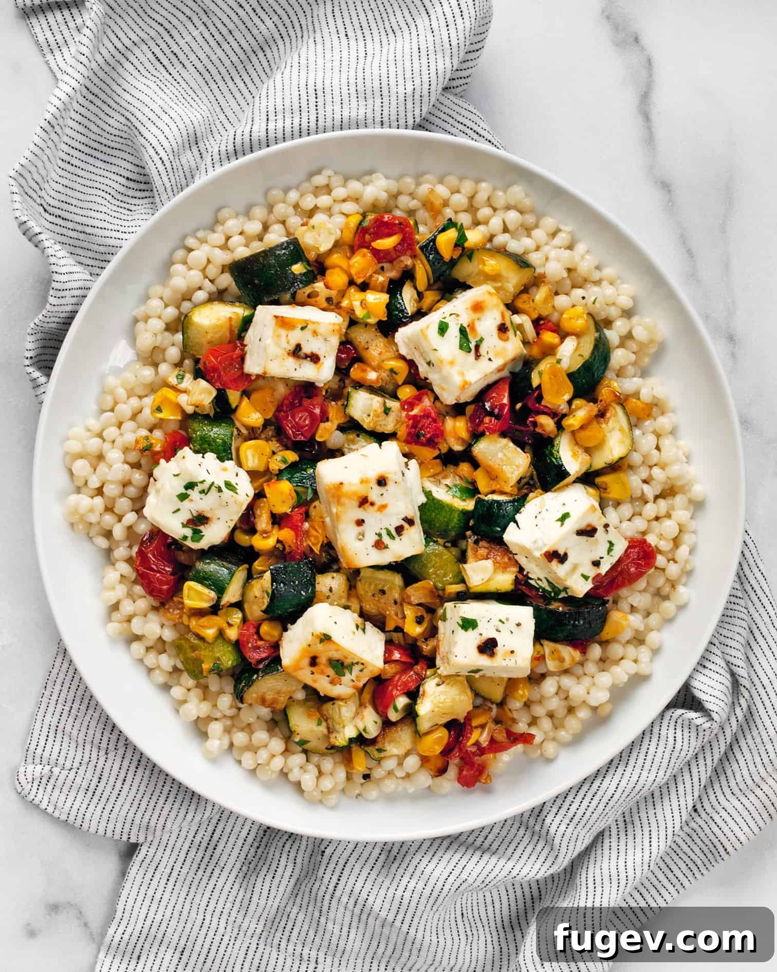Tek Tepside Fırınlanmış Feta ve Sebzeler 6 A beautifully plated serving of baked feta with roasted vegetables and pearl couscous, ready to be enjoyed.