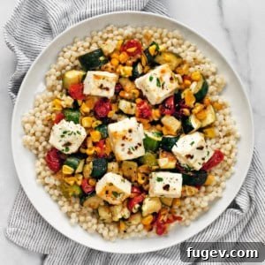 Baked feta with corn, tomatoes and zucchini with pearl couscous on a plate, a delicious and easy one-pan meal.
