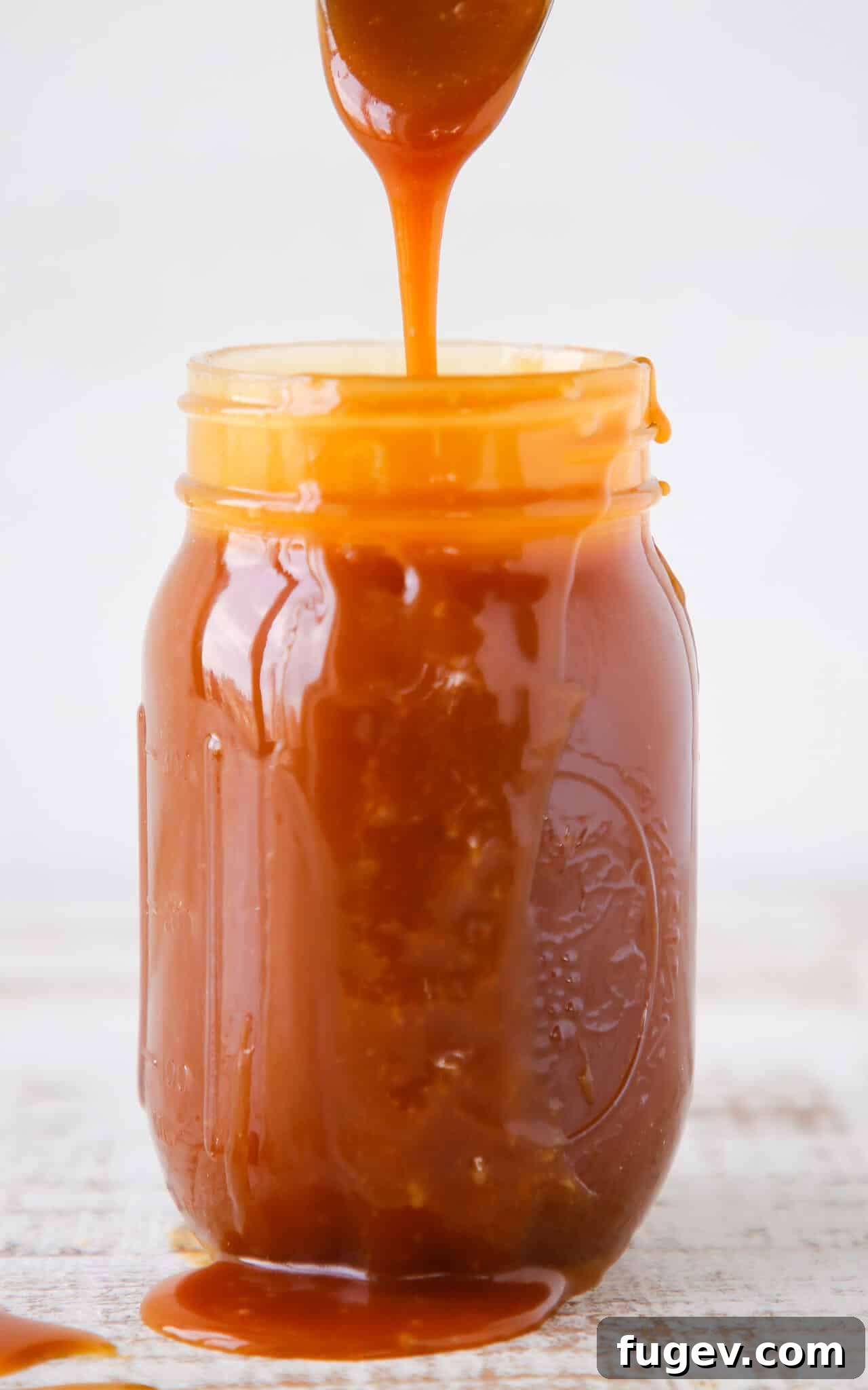 Salted Caramel Drizzle 2 Homemade salted caramel sauce pouring from a spoon into a glass jar.