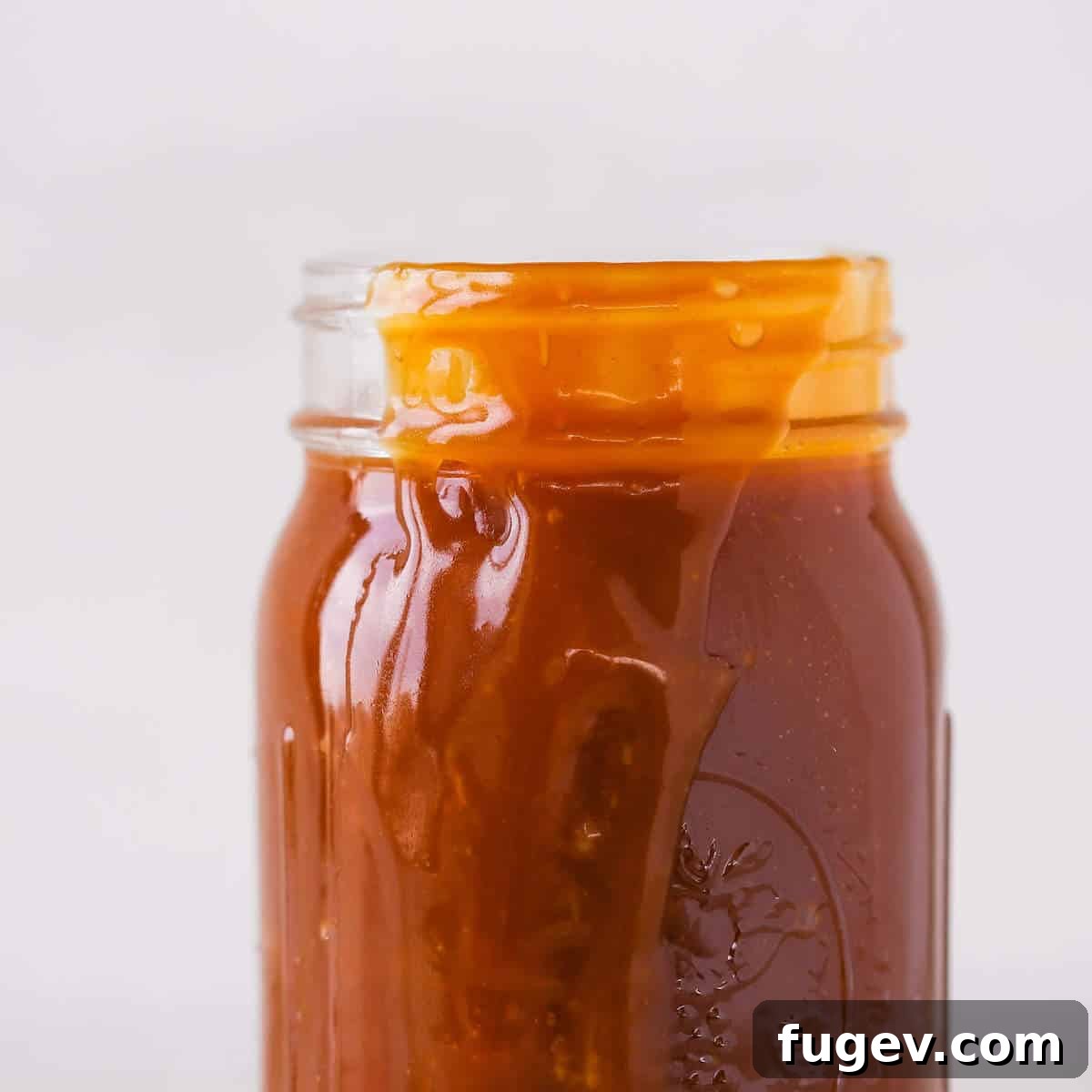 Salted Caramel Drizzle 4 Salted caramel sauce spilling over the side of a glass jar, highlighting its thick texture.