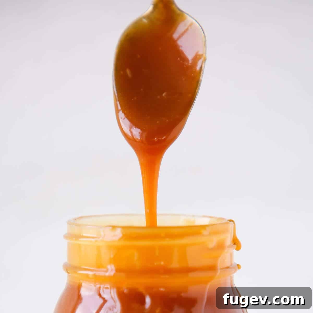 Salted Caramel Drizzle 5 Thick salted caramel sauce dripping from a spoon, showcasing its rich texture.