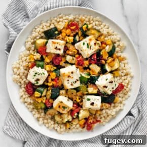 Baked feta with corn, tomatoes and zucchini with pearl couscous on a plate.