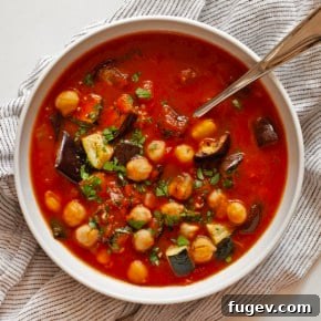 A comforting bowl of thick roasted eggplant, zucchini, and tomato stew, garnished with crumbled feta cheese.