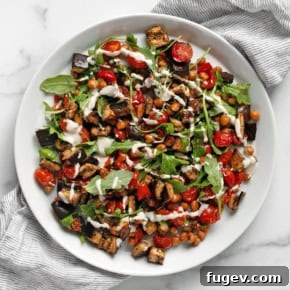 Roasted eggplant, juicy tomatoes, and crispy chickpeas drizzled with a creamy lemon tahini sauce on a plate.