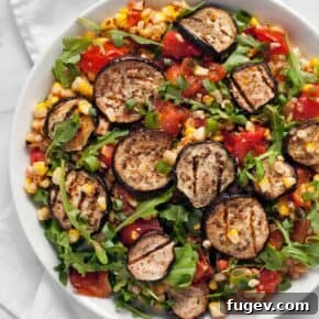 A vibrant platter of grilled eggplant slices, sweet corn kernels, and fresh tomatoes, tossed with a savory dressing.