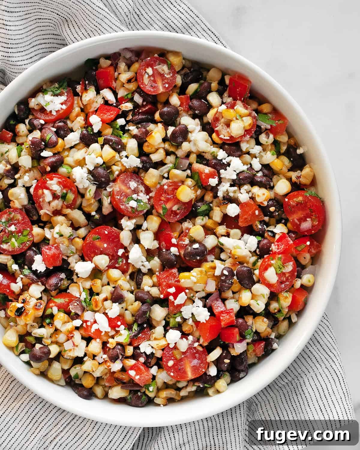 Southwestern Black Bean and Corn Medley 6 Close-up shot of grilled corn black bean salad in a light blue bowl, garnished with a lime wedge and cilantro, highlighting the textures and colors of the ingredients.