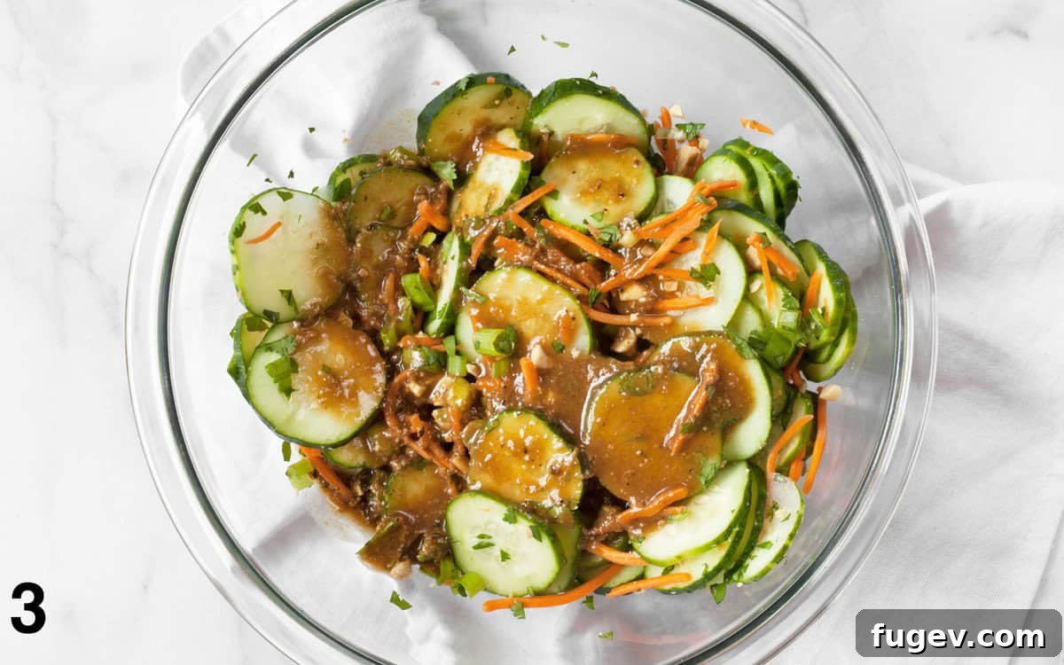 Asian Cucumber Salad tossed evenly with creamy peanut dressing in a mixing bowl, ready for serving.