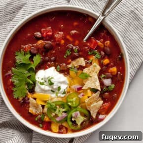 Bowl of smoky black bean chili with tortilla chips, sour cream, cilantro and cheese as toppings.