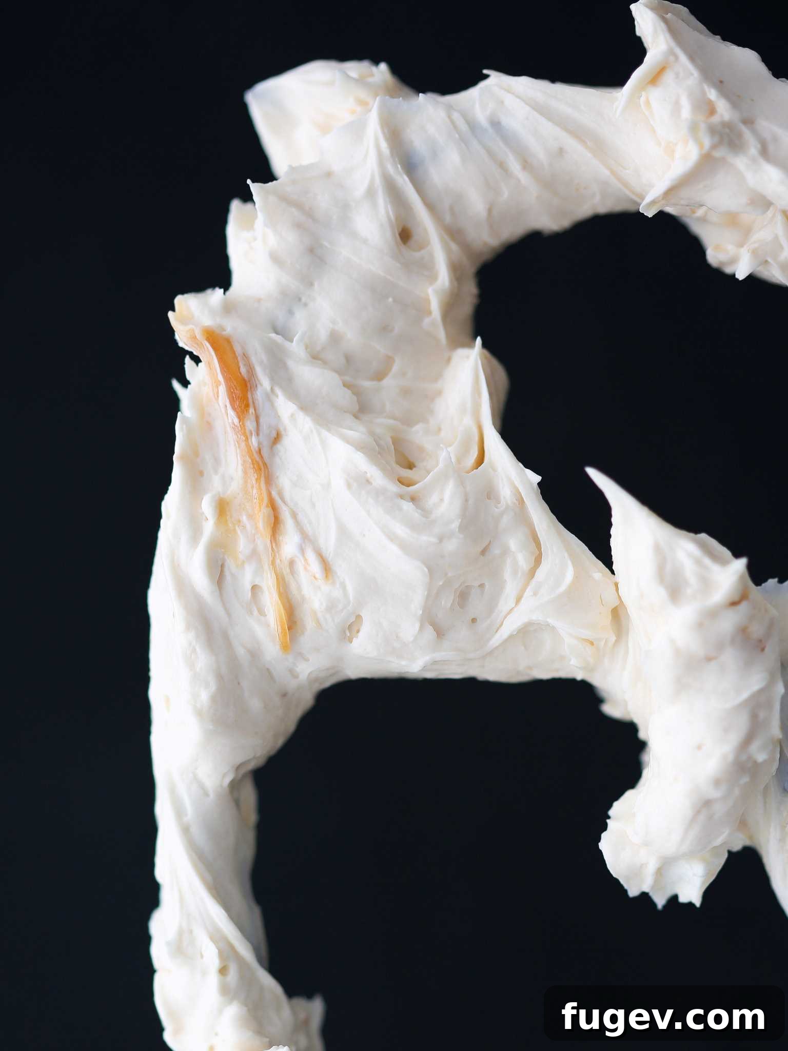 Caramel Swiss Meringue Buttercream on a black background, showcasing its smooth texture.