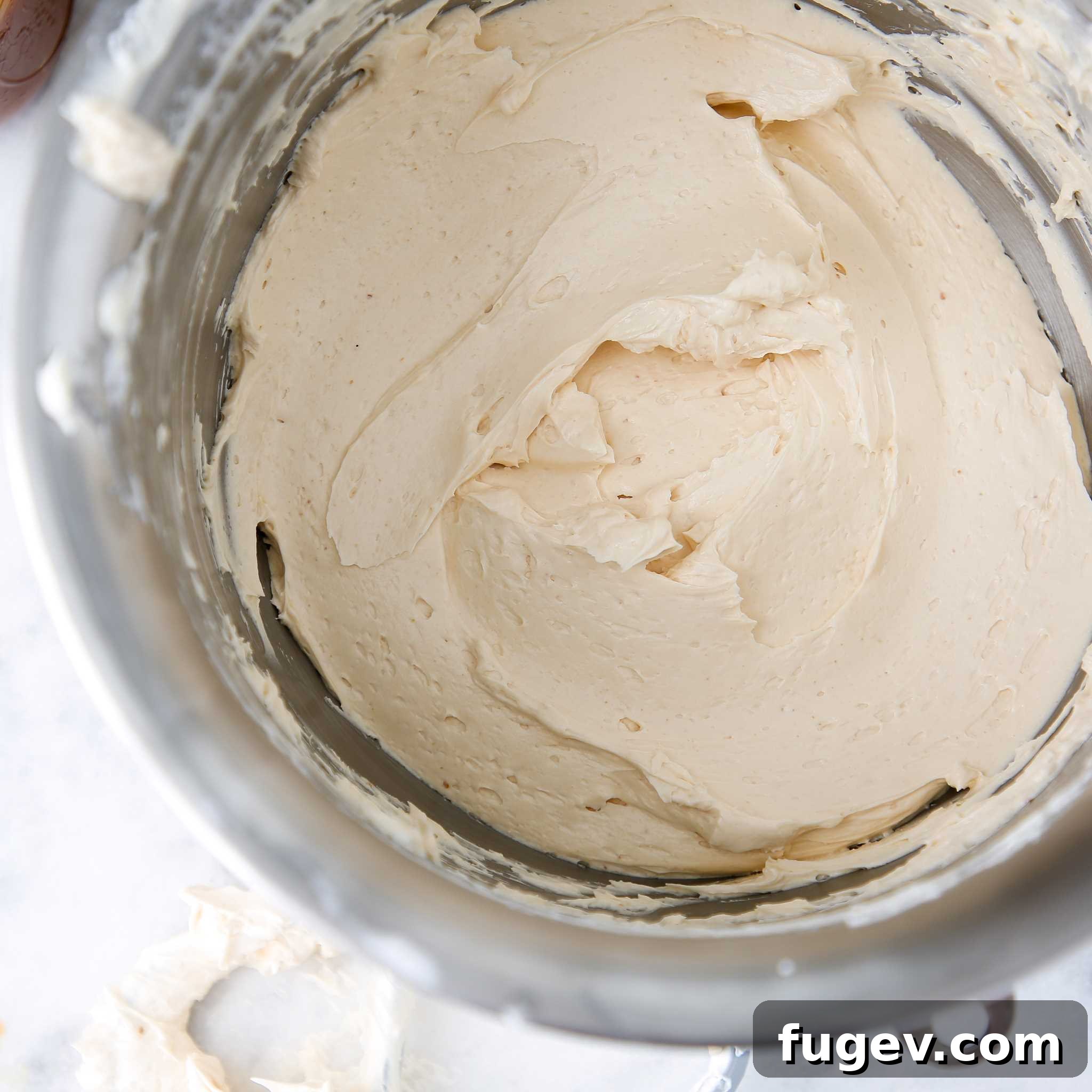 Caramel Swiss Meringue Buttercream being mixed in a large bowl, showing its creamy texture.