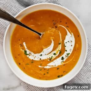 Bowl of turmeric butternut squash apple soup with a yogurt swirl and fresh herbs.