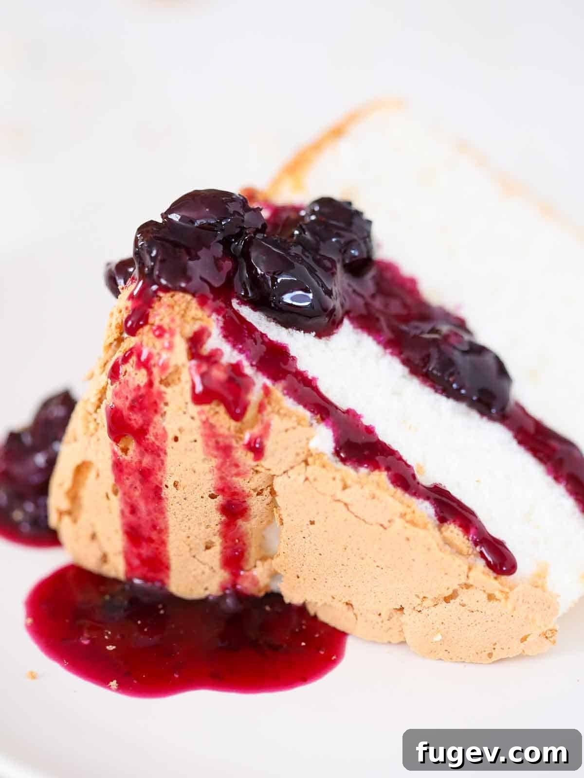 Heavenly Cloud Delight 3 A perfectly sliced angel food cake on a white plate, generously topped with a vibrant blueberry sauce, creating a delectable pool around the base.