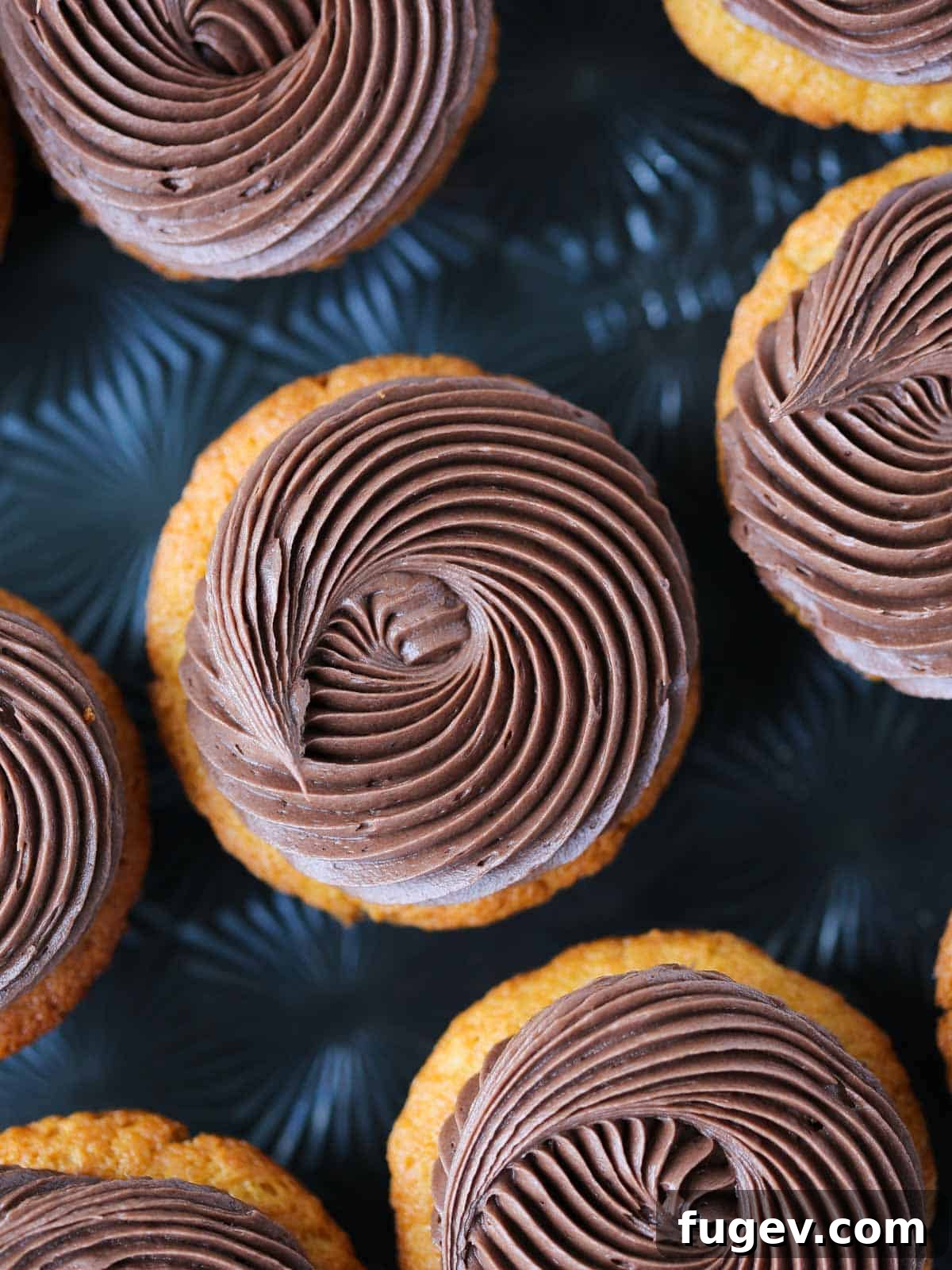 Gooey Chocolate Caramel Dreams 2 Swirls of rich chocolate buttercream frosting on golden caramel cupcakes, presented against a sophisticated black background, highlighting their decadent appeal.