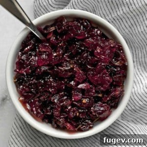 A close-up of a bowl of homemade onion jam with a spoon, highlighting its rich texture and color.