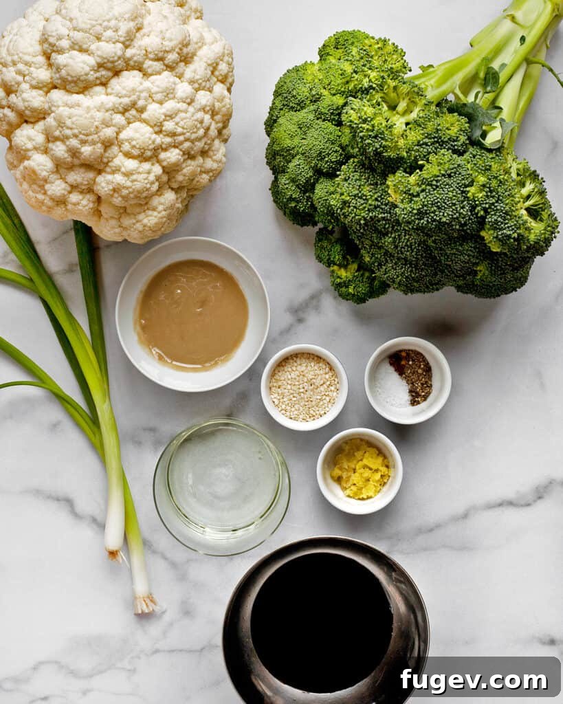 Golden Tahini Roasted Florets 3 A flat lay image showing fresh broccoli, cauliflower, a bowl of tahini, soy sauce, fresh ginger, and garlic cloves, ready for the recipe.