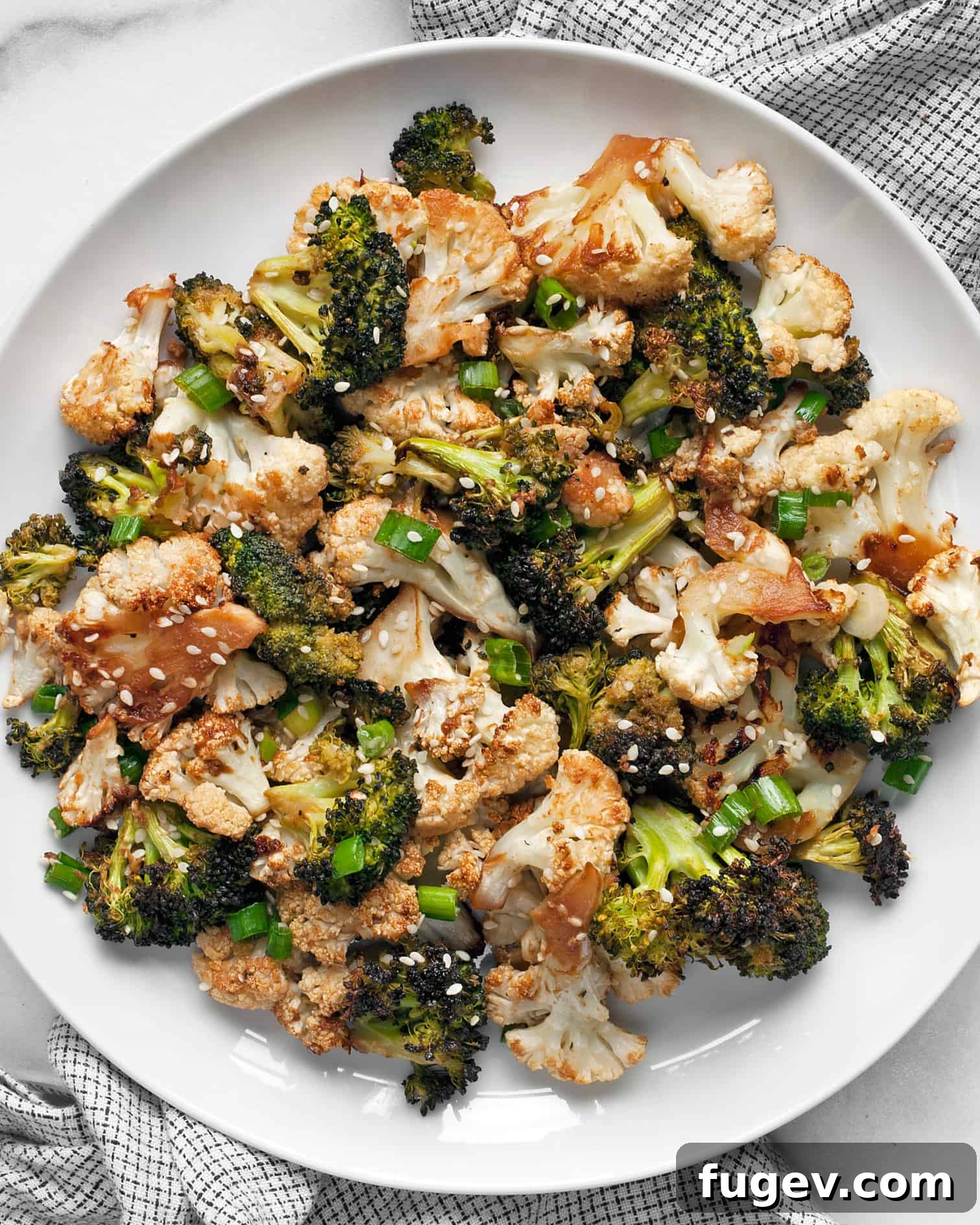 Golden Tahini Roasted Florets 6 A serving bowl filled with Tahini Roasted Broccoli and Cauliflower, garnished with scallions and sesame seeds.