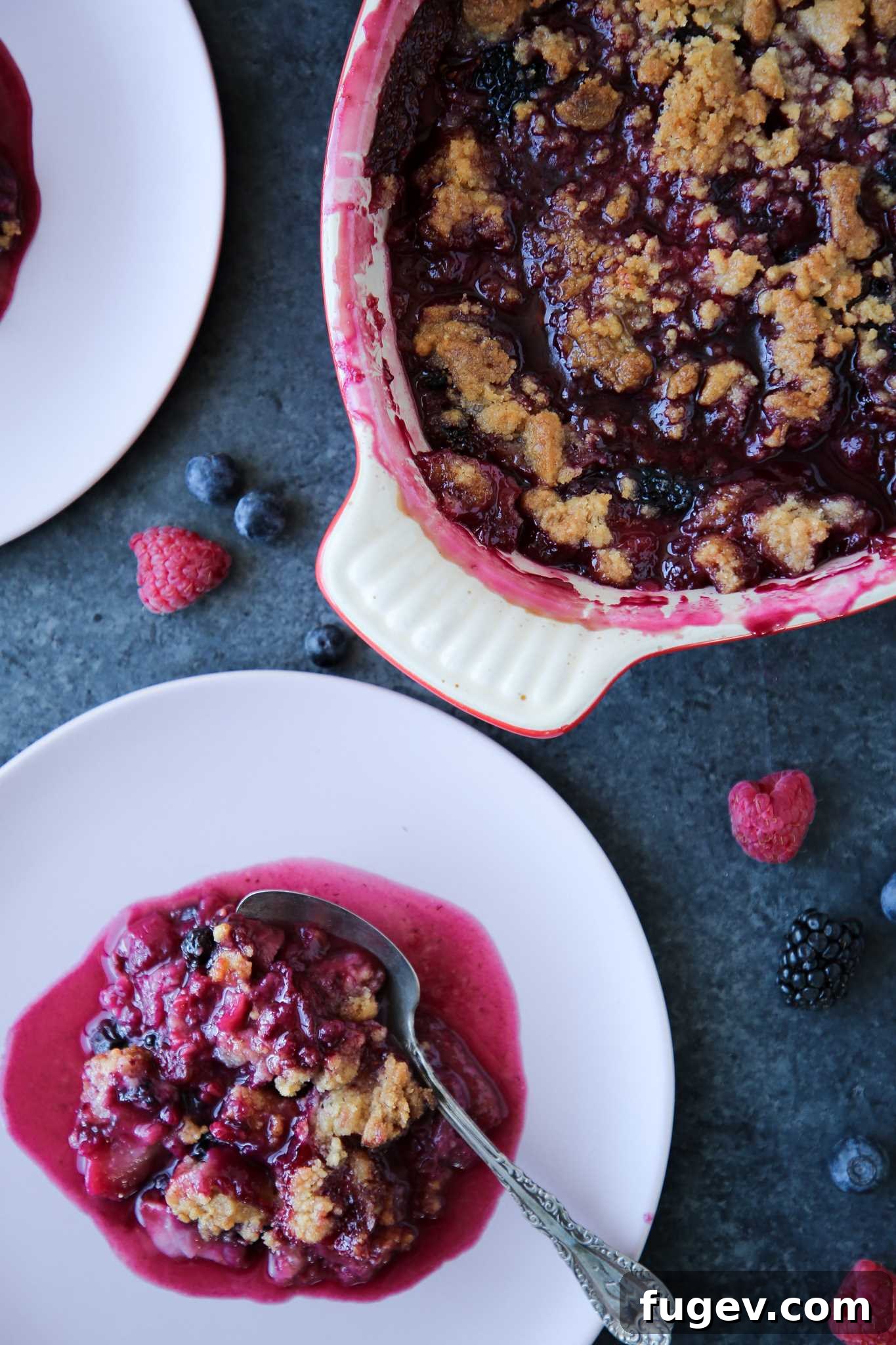 Irresistible Berry Crumble 2 Berry crumble in white baking dish on blue background, garnished with fresh berries.