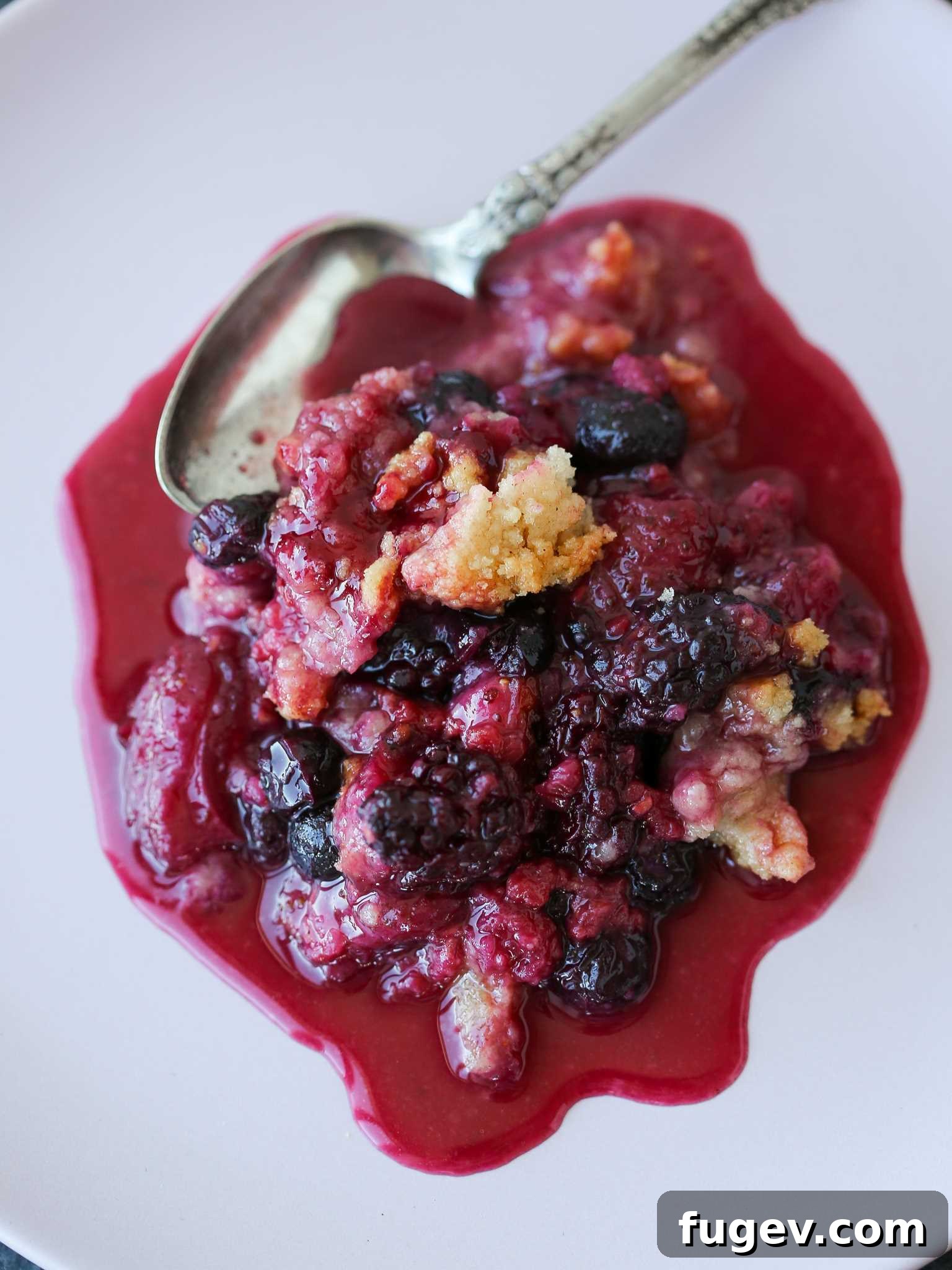 Irresistible Berry Crumble 3 Mixed berry crumble served on a white plate with a spoonful missing.
