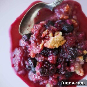 Mixed berry crumble with a silver spoon, showcasing the crumbly topping and juicy fruit.