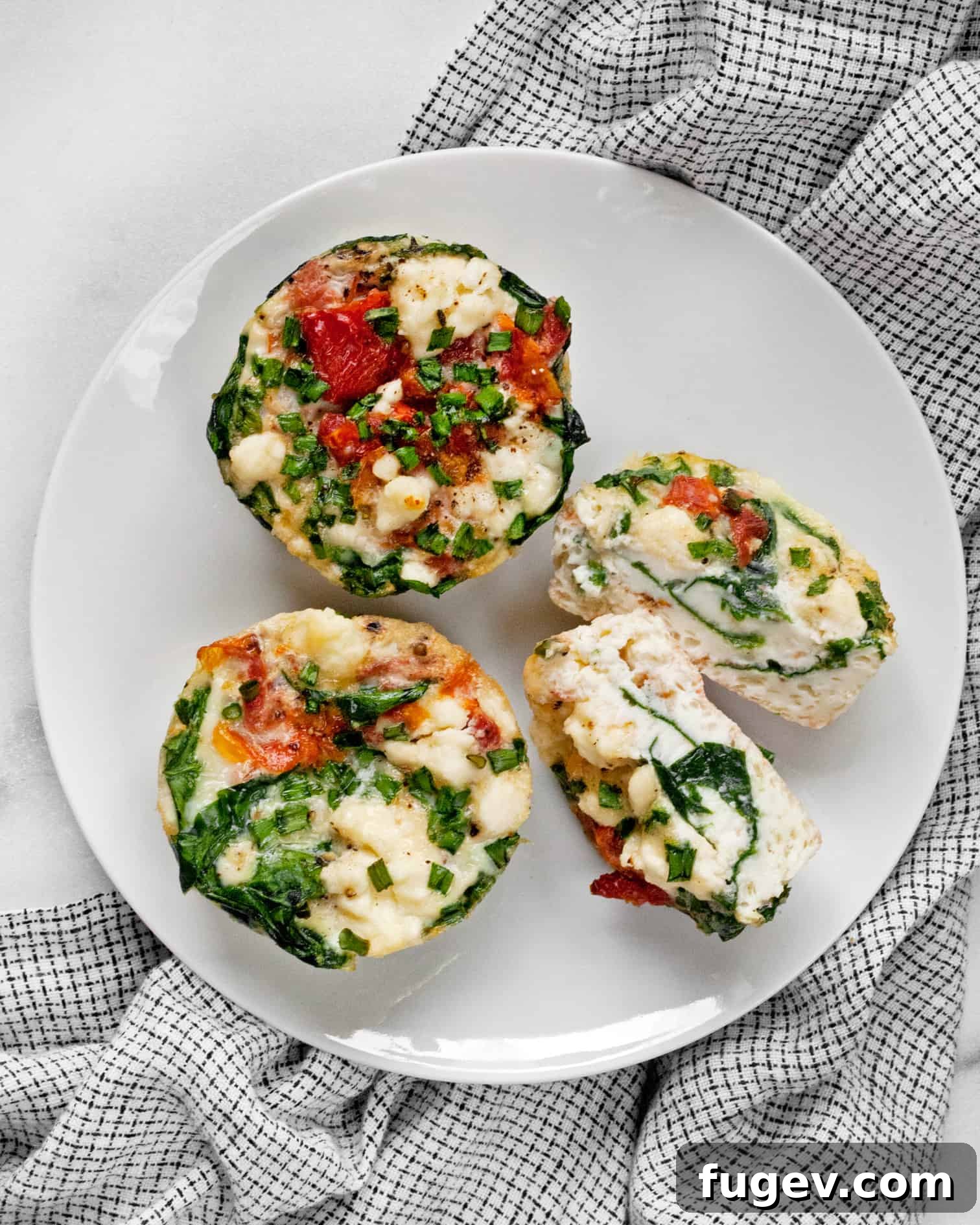 Fluffy Spinach Feta Protein Poppers 2 Three spinach feta mini frittatas on a plate with one cut in half, showcasing the vibrant ingredients.