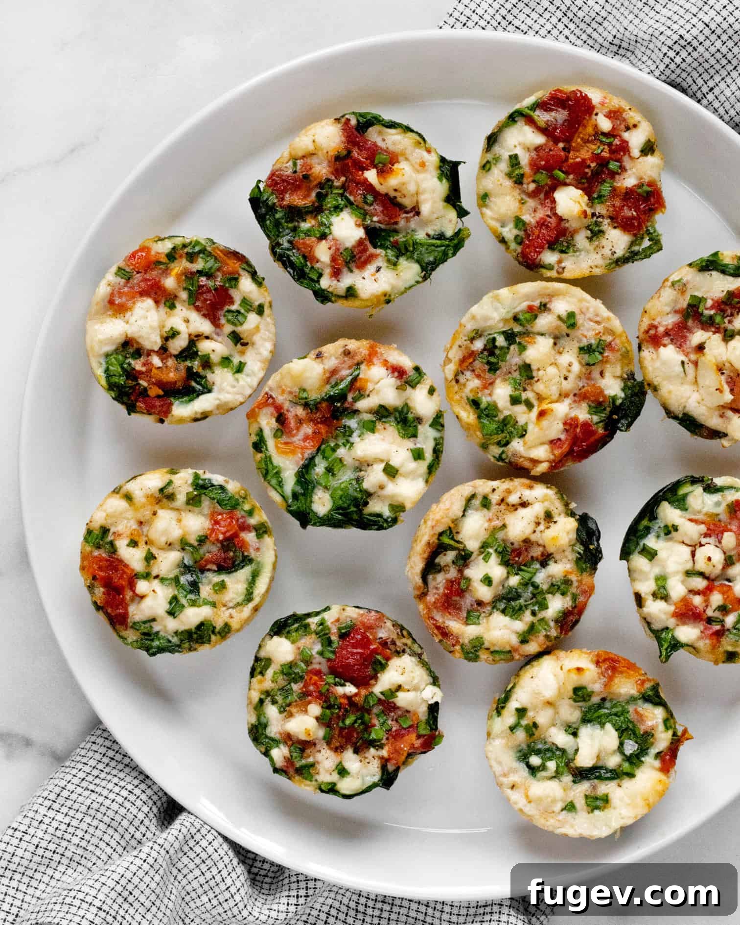 Fluffy Spinach Feta Protein Poppers 6 A close-up of several spinach feta egg white bites arranged artfully on a white plate, highlighting their appetizing texture and ingredients.