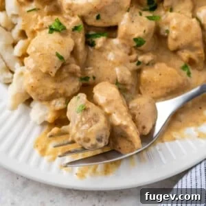 Close-up of chicken paprikash with parsley on a white plate, showing a fork taking a bite.